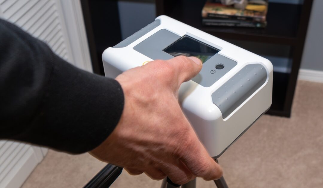 A closeup of a person's hand touching a radon testing device. The device is near a closet and a shelf.