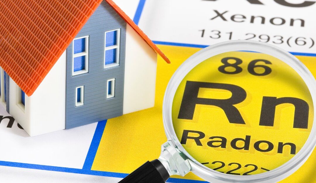 A mini plastic home on a periodic table beside the box for radon. There is a magnifying glass lying over the symbol for radon.