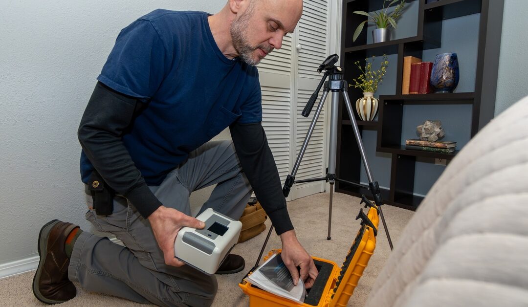 A home inspector wearing a blue shirt kneeling down to set up a radon test in a residential bedroom.