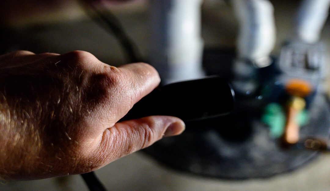 A person holding a flashlight in a basement. They are aiming the flashlight at a sump pump in the corner.